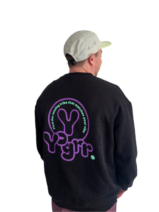 Person wearing a black sweatshirt with a purple graphic on the back against a white wall.