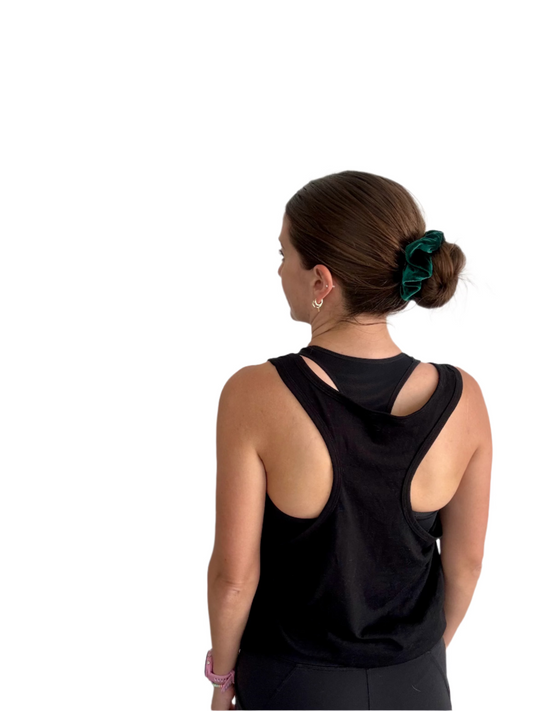 Person wearing a black sleeveless top with a green hair accessory against a plain background